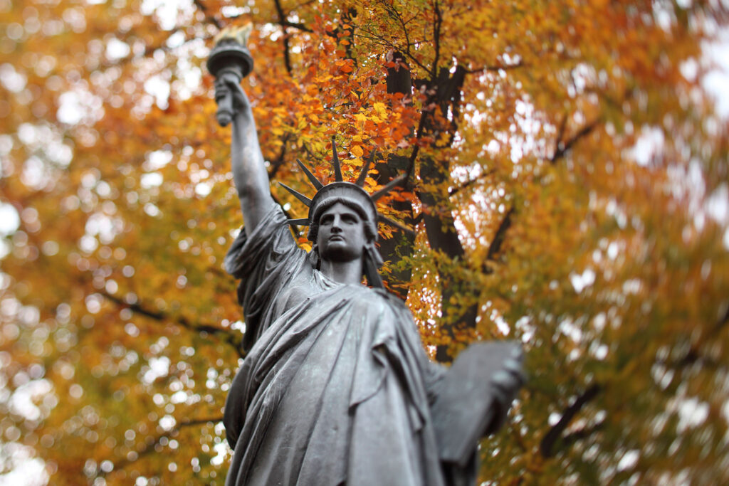 Estátua da Liberdade em Paris diante de folhas outonais claras.