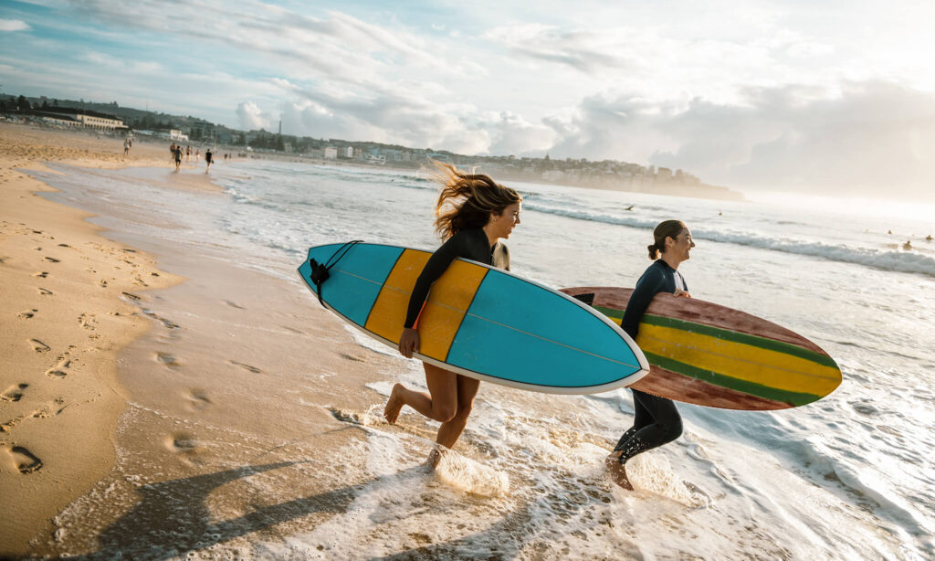 Dois rapazes correm pela praia com suas pranchas de surfe.