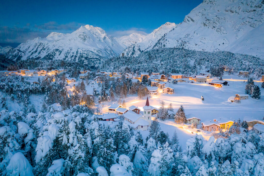 Vila suíça idílica com luzes amarelas suaves cercada de montanhas alpinas e coberta de neve.