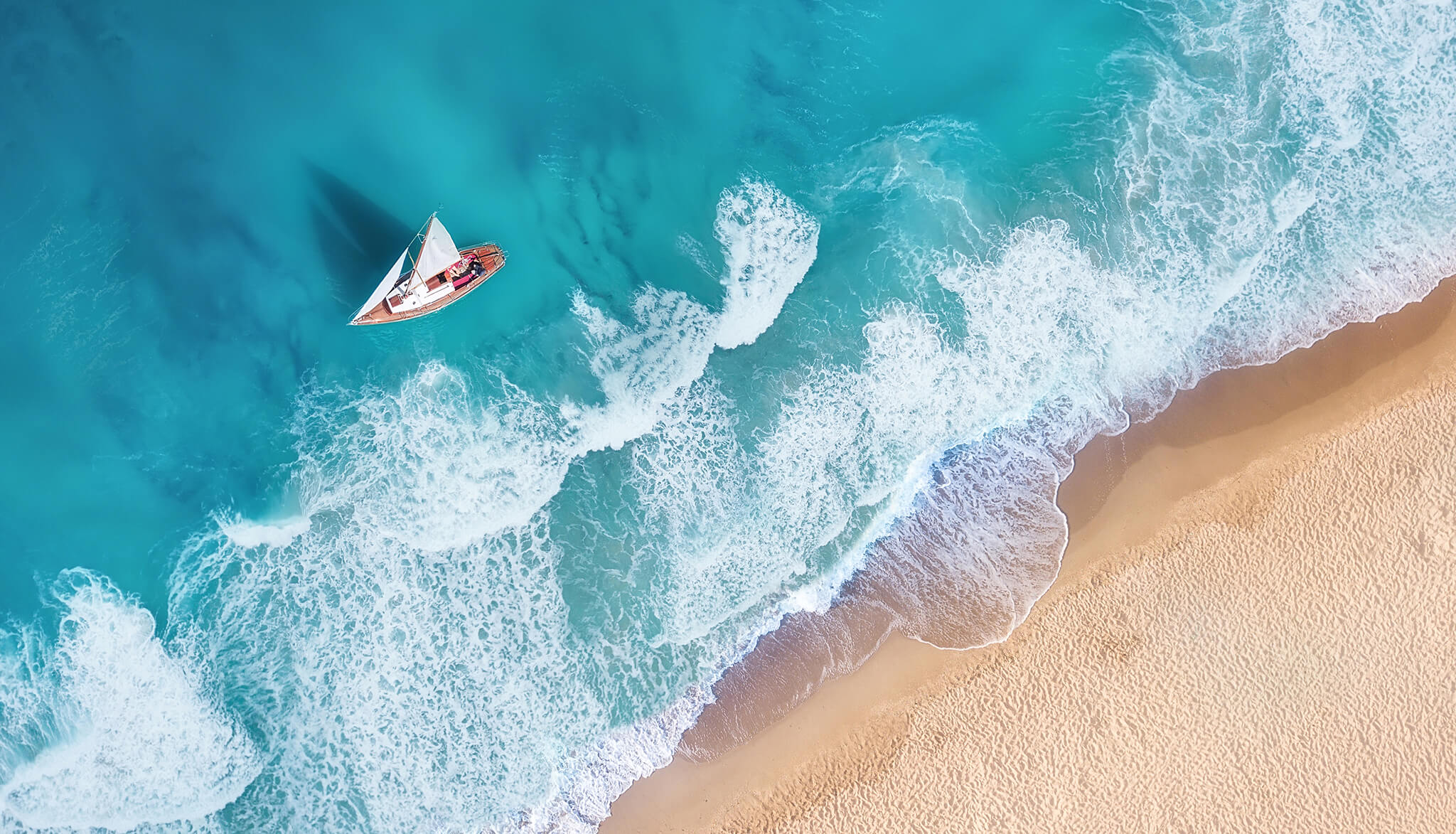 Barco à vela desliza desviando-se das ondas em uma ilha caribenha.