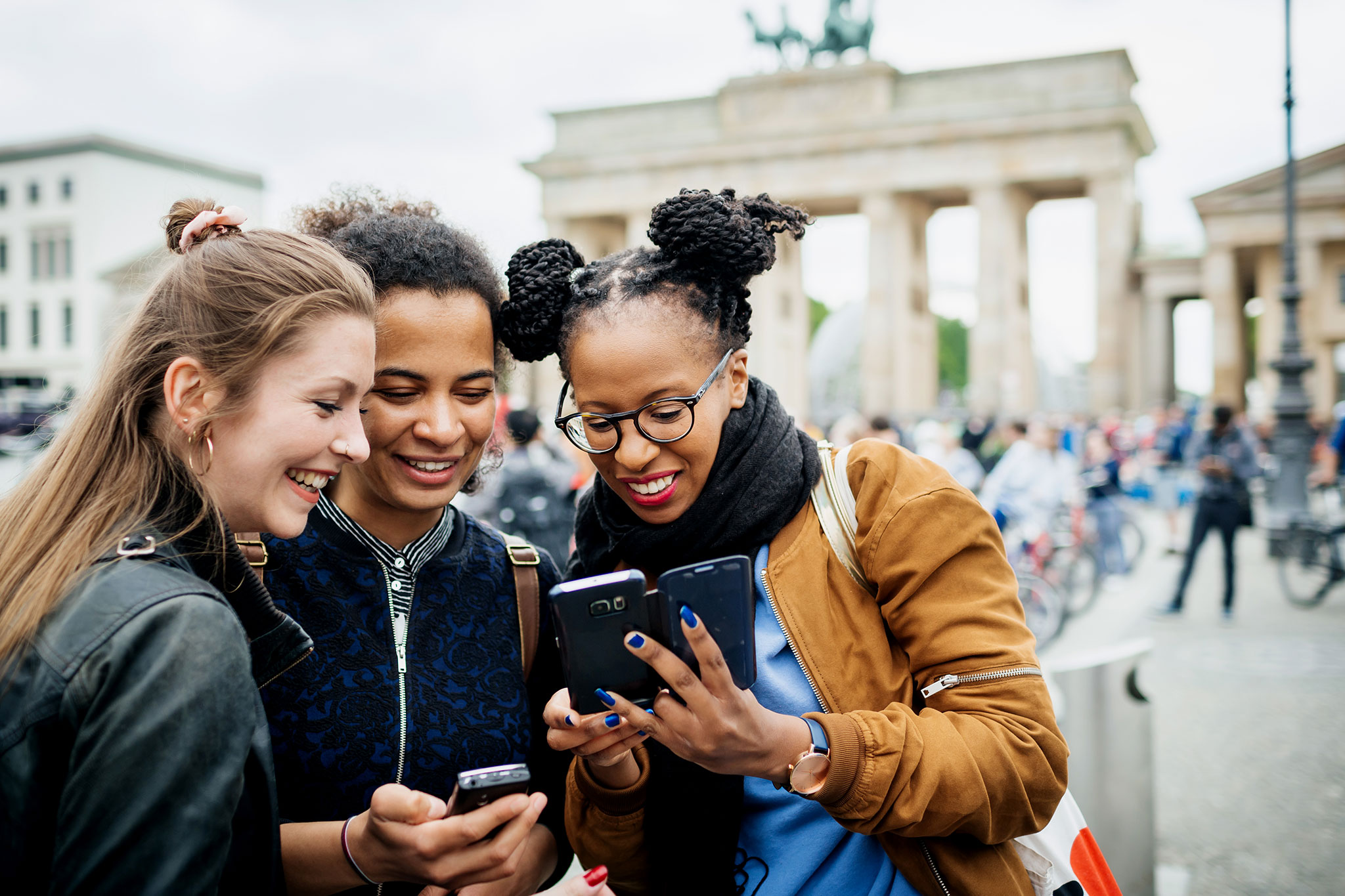 Três moças em visita a Berlim param para olhar fotos recentes no celular.