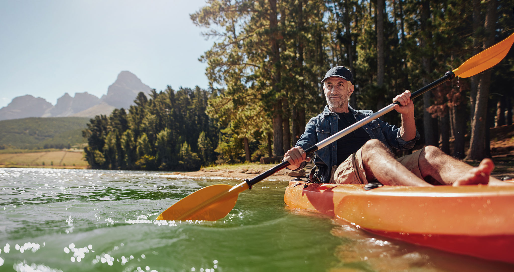 Homem de meia idade com short rema de caiaque em um lago.