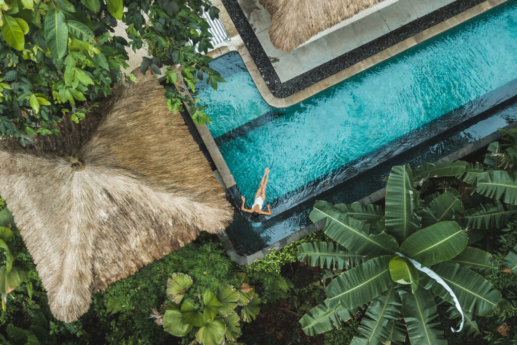 Vista aérea de uma mulher em uma piscina cercada de plantas tropicais.