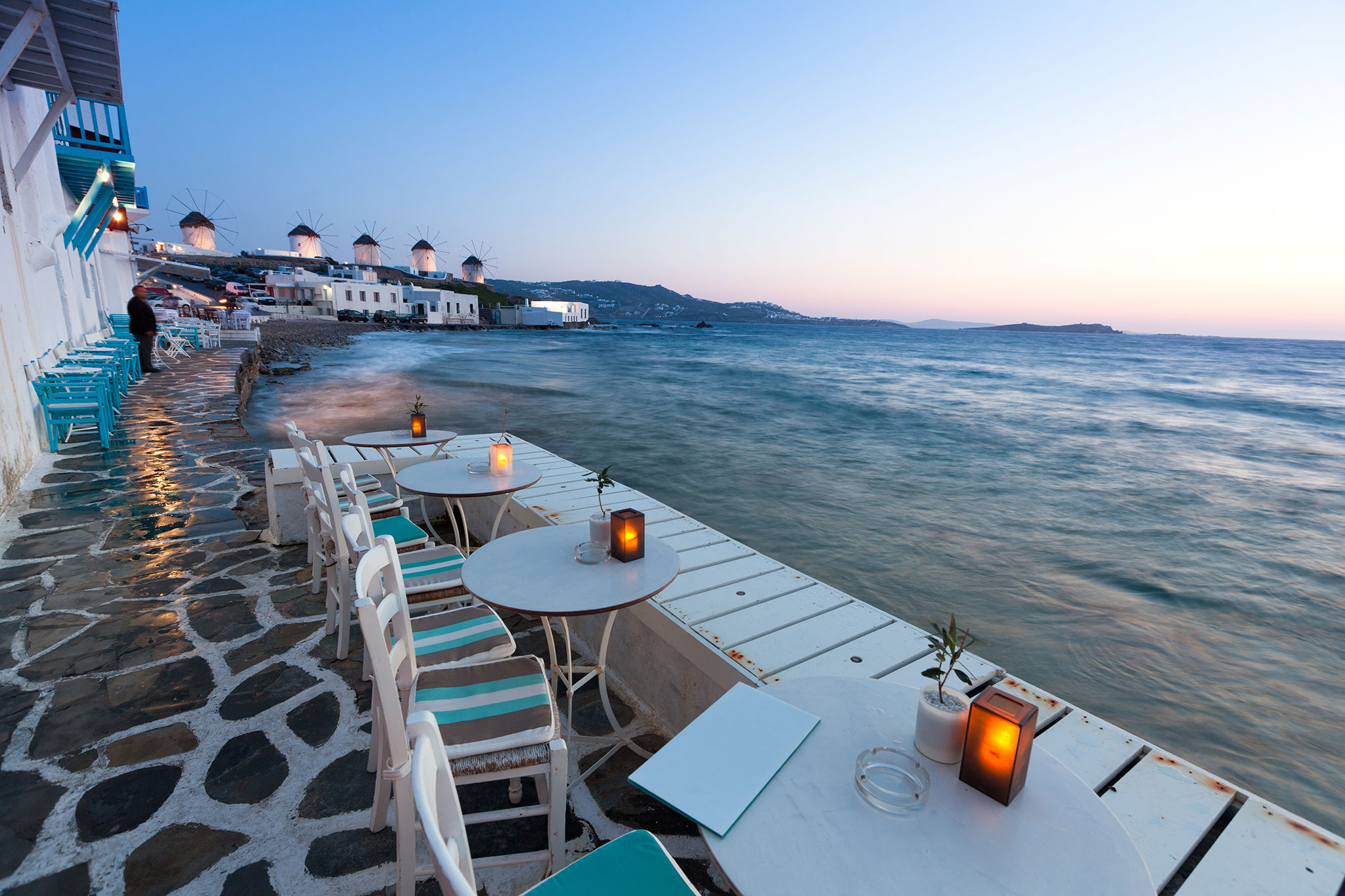 Mesas e cadeiras com vista para o Mediterrâneo no ocaso de Mykonos.