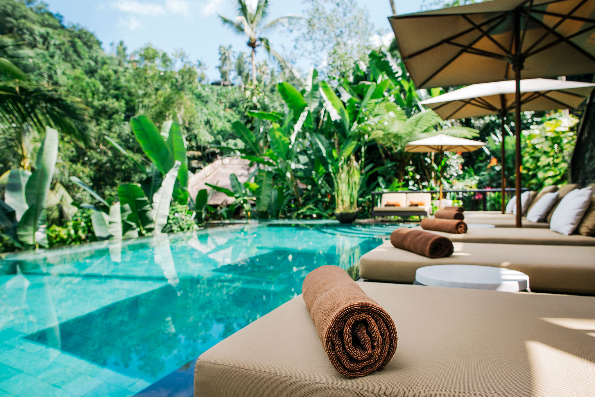 Toalhas limpas e macias em espreguiçadeiras aguardam os hóspedes ao lado de uma piscina tropical.