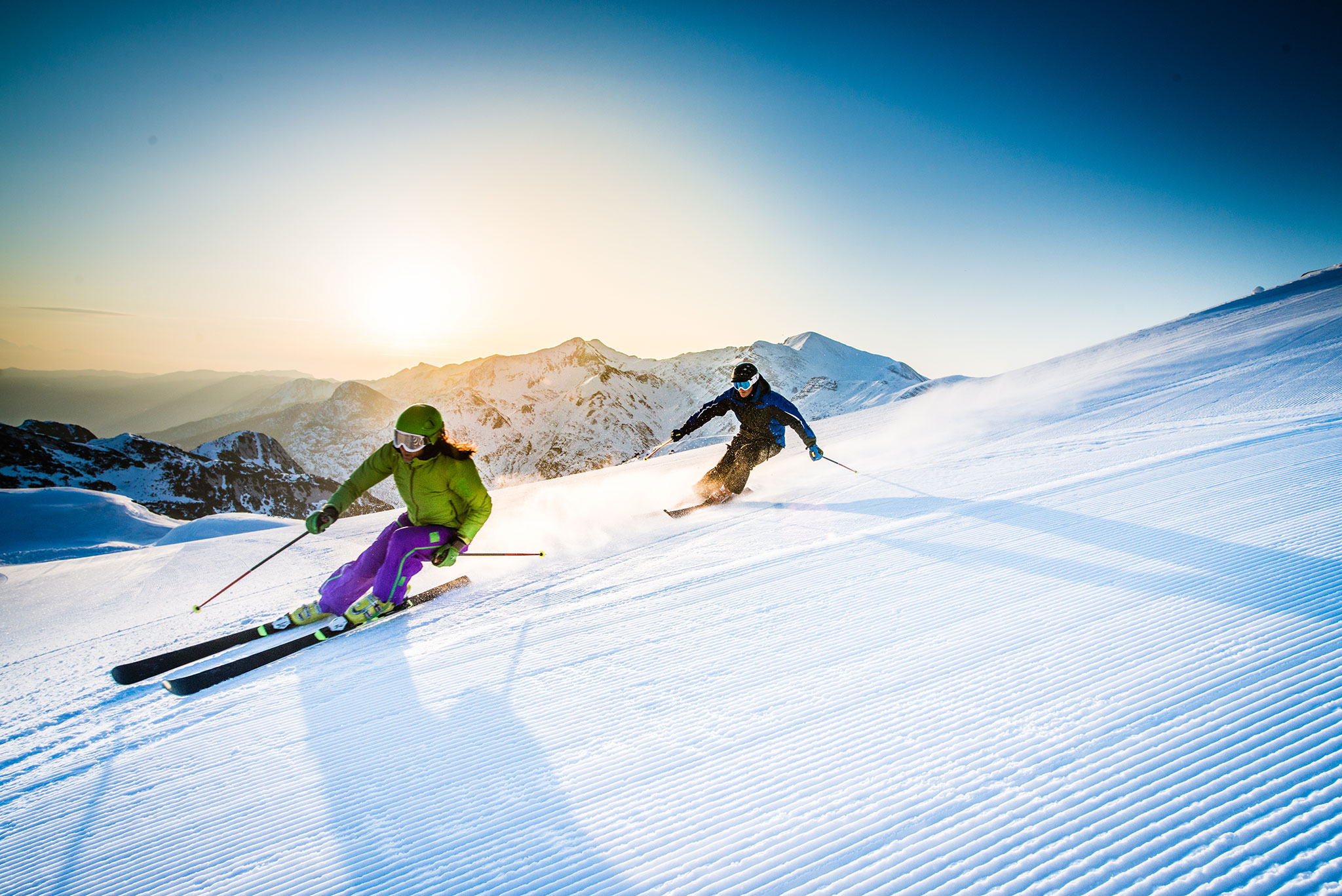 Dois esquiadores se inclinam em uma curva sobre a neve fresca.