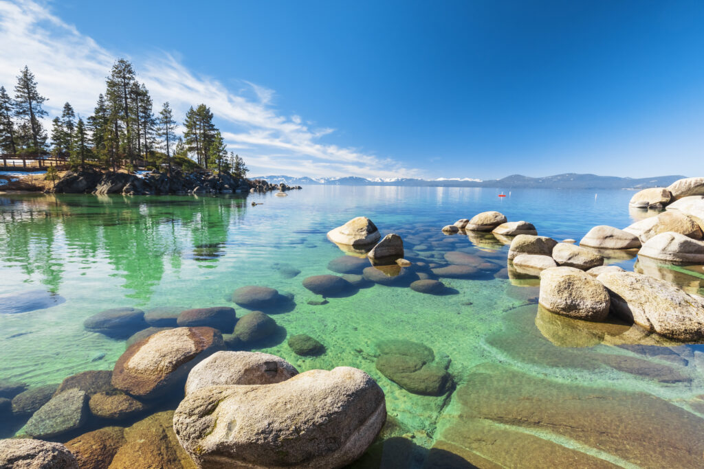 A costa rochosa de Lake Tahoe em um dia de sol, praia com céu azul sobre água transparente